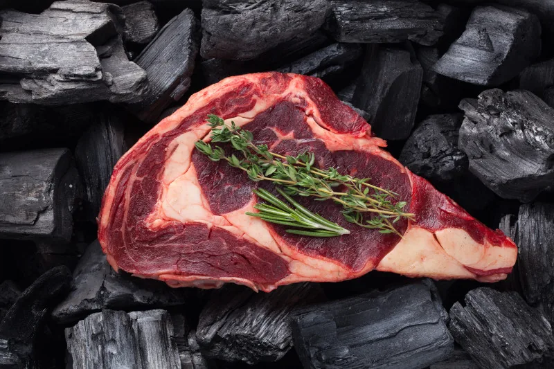 Rohes Steak präsentiert auf Holzkohle, bereit zum gegrillt werden
